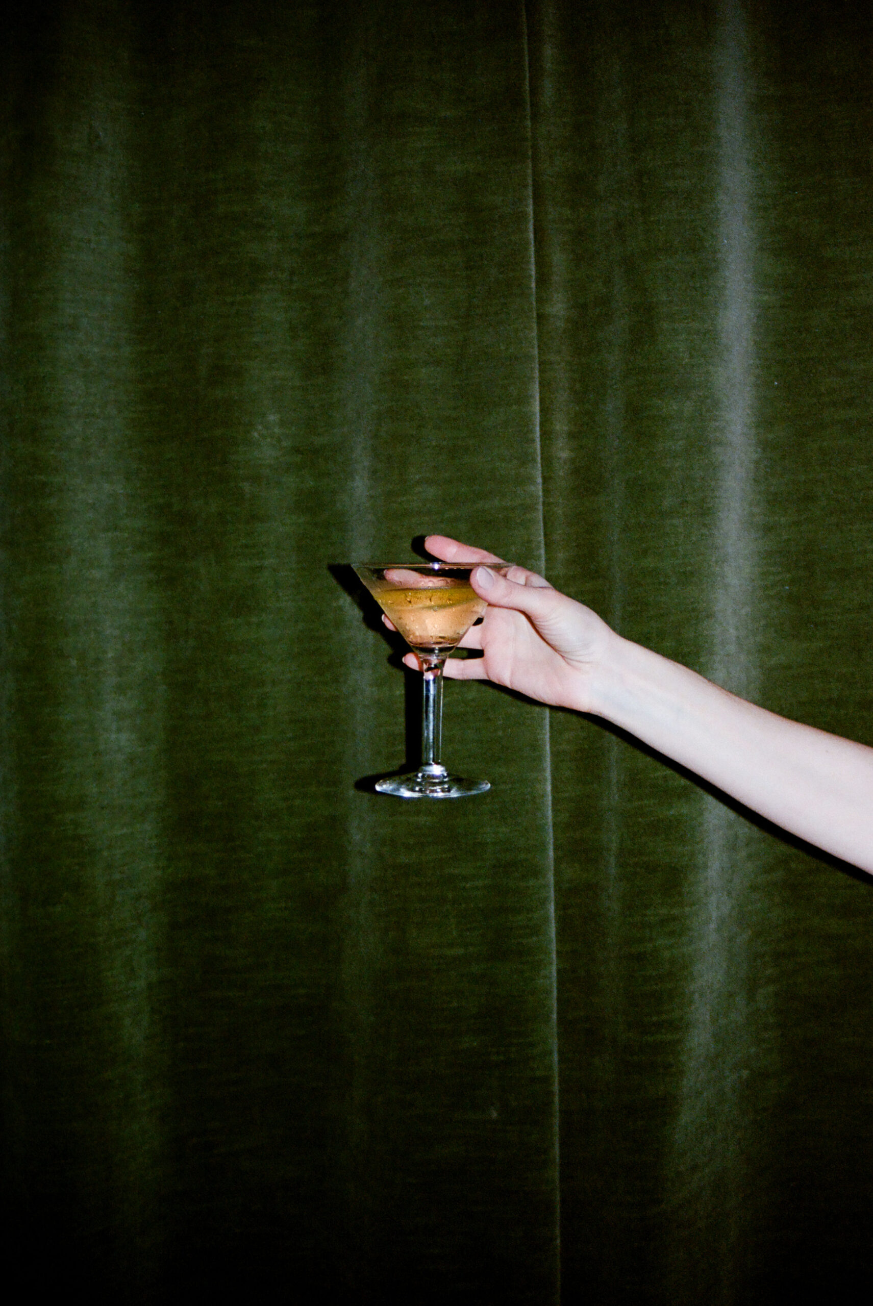 bowery hotel party hand holding martini glass against green velvet curtains shot on film by parkers pictures